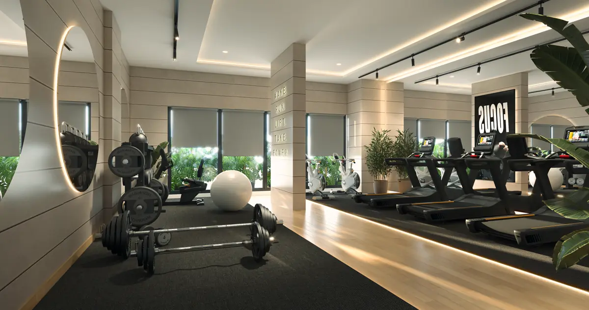 The gym, with a rack of dumbbells in the foreground and cardio equipment along a glazed wall.